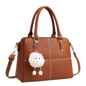 Brown leather handbag with white stitching and cute plush monster charm on white background