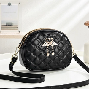 Quilted black crossbody bag with gold swan pendant and pearl details on a desk