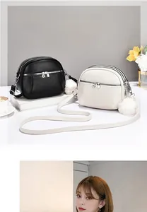 Detail of round crossbody bags in black and cream featuring triple zippers and plush pom poms