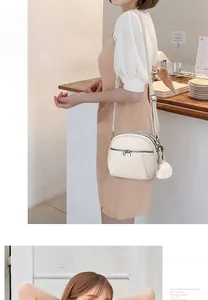 Detail of off-white faux leather crossbody bag with triple zippers and plush ball charm