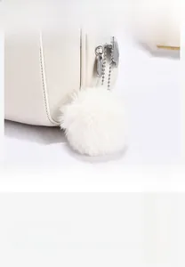 Detail showing white fluffy pom-pom charm and polished teardrop metal zipper puller