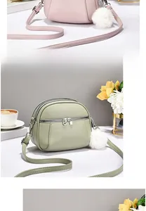 Detail of round soft leather crossbody bag with multiple zippers and plush ball charm