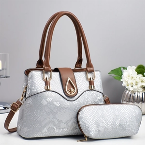 Detail view of silver snake-embossed handbag set with gold hardware and brown leather handles