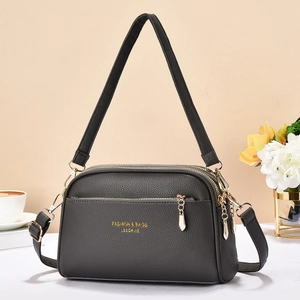 Dark grey lychee leather crossbody bag with triple zippers on marble background
