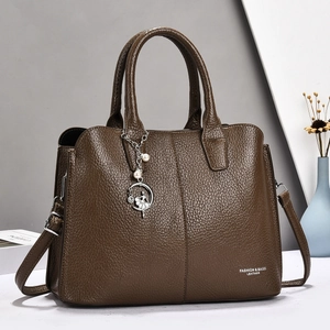Detail of dark brown pebble leather handbag featuring pearl charm and adjustable strap