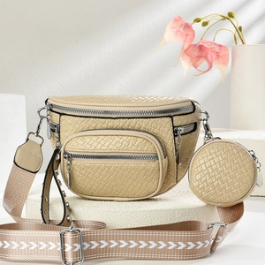 Beige faux crocodile leather crossbody bag with patterned wide strap on a stone base