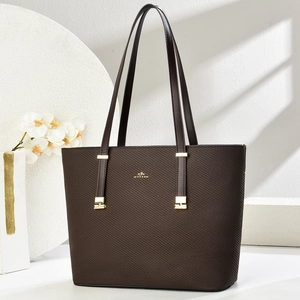 Brown cross-grain leather tote bag with gold hardware and shoulder straps on a clean set