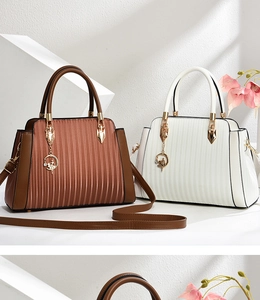Detail of pleated leather texture and gold dancer pendant on dual-color handbags