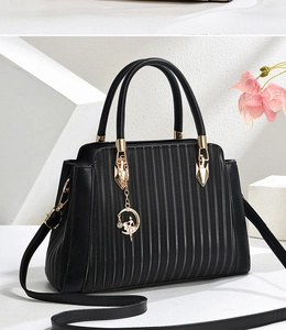 Macro view of black leather handbag with pleated texture and golden ballerina pendant