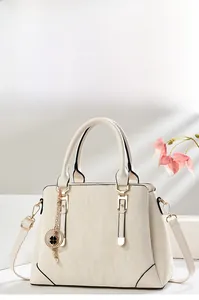 Close-up of textured cream handbag with gold buckle, shoulder strap and clover charm
