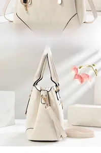Detail view of cream tote bag featuring clover metal charm and pearl pendant accents