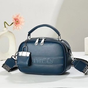 Close-up of a dark blue textured leather crossbody bag with striped wide strap and mini charm