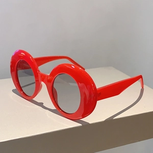 Detail view of bold red round frame sunglasses with dark lenses on a minimalist pedestal