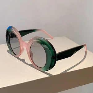 Detail view of pink and dark green gradient round frame sunglasses on white pedestal