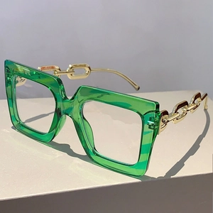 Close-up of square green frames with gold chain temples on minimalist gray stand