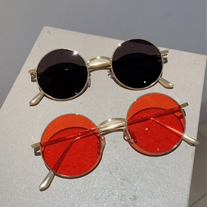 Retro round metal sunglasses in black and red lenses with gold frames on stone stand