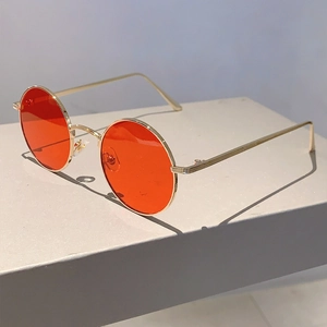 Detailed side view of round sunglasses featuring gold metal frame and red tinted lenses