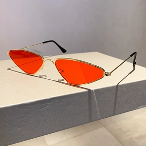 Macro view of orange triangle lenses and sleek gold metal frame sunglasses on a gray stand