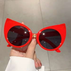 Detail of red cat-eye sunglasses featuring golden cross metal bridge and black lenses