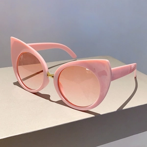 Detail of pink cat-eye sunglasses with gold metal cross bridge on a grey display stand