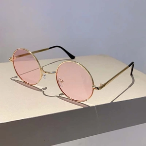 Lunettes de soleil rondes rétro avec verres roses et monture dorée sur support minimaliste
