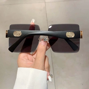 Detail of rimless gradient sunglasses featuring a gold rose relief on wide black temples