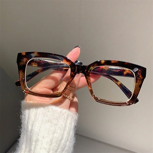 Detail of square oversized tortoiseshell frame glasses held in hand showing retro pattern