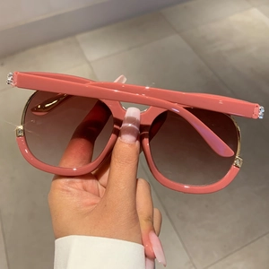 Detail of pink frame sunglasses featuring golden metal inner rim and rhinestone accents