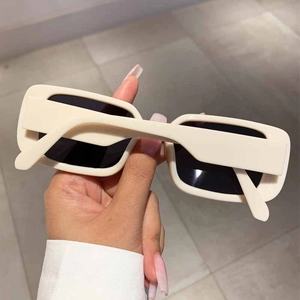 Close-up of cream square sunglasses with thick frames and dark lenses held by hand