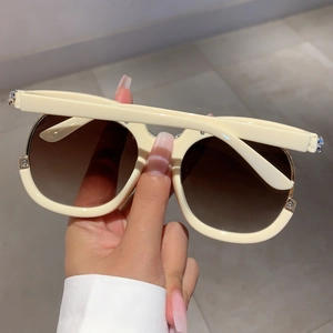 Detail shot of cream white oversized sunglasses featuring brown gradient lenses and metal hinges