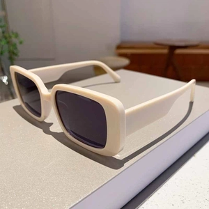 Detailed close-up of retro square cream sunglasses with thick frames on a display stand