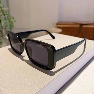 Detail of square black frame sunglasses on a white pedestal with soft indoor lighting