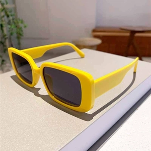 Side view of trendy bright yellow rectangular sunglasses with dark lenses on a white block