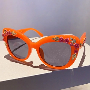 Detail of orange cat eye sunglasses featuring 3D pink floral and gold leaf decorations