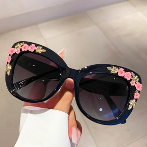 Close-up of black floral cat-eye sunglasses with pink 3D flowers and gold leaf accents