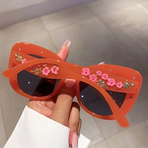 Detail view of orange cat-eye sunglasses featuring pink enamel flowers and gold leaves