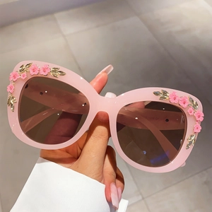 Close-up of pink cat-eye sunglasses with detailed 3D floral and golden leaf accents