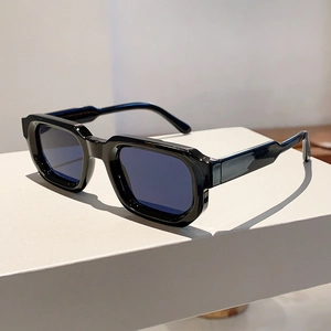 Détail de lunettes de soleil carrées avec monture noire épaisse sur un socle blanc