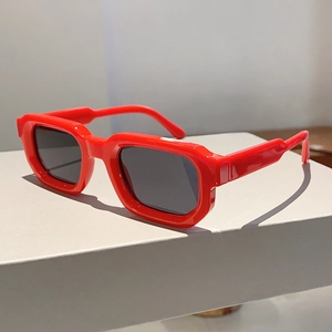 Détail de lunettes de soleil carrées rouges avec monture épaisse en résine et verres noirs foncés