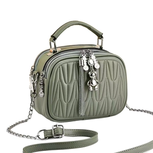 Quilted green leather crossbody bag with chain strap and teddy bear pendant detail