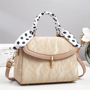 Detail of cream crossbody bag with pleated texture, gold twist lock and polka dot scarf