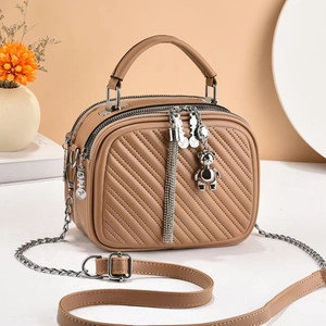 Detail of khaki crossbody bag featuring diagonal quilting, metal tassel, and bear charm