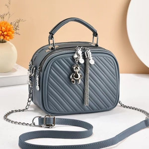 Close-up of blue quilted crossbody bag with triple zippers and bear tassel charm