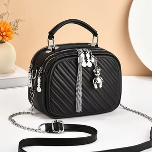 Detail of black quilted crossbody bag with silver chain strap and bear charm pendant