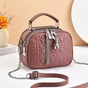 Detail of dusty pink PU leather handbag with heart quilting and cute bear charm pendant