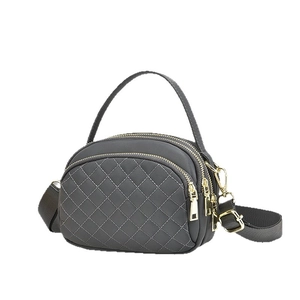 Deep grey quilted crossbody bag with triple zipper layers and gold hardware on white background