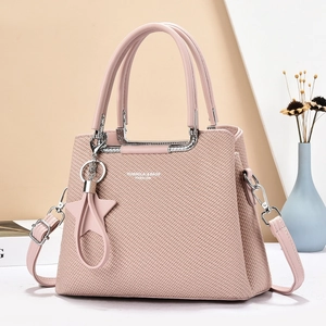 Détail d'un sac à main rose tressé avec poignées en métal argenté et pendentif