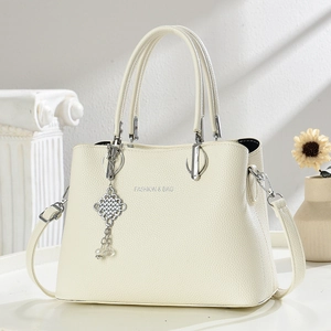 Détail d'un sac à main crème élégant avec motif litchi et pendentif en métal argenté