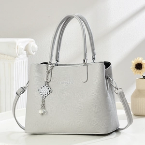 Detail view of light grey pebble-grain handbag with elegant pearl tassel and silver charms