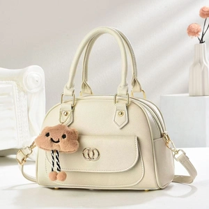 Detail of minimalist cream leather satchel featuring gold hardware and a cute plush charm